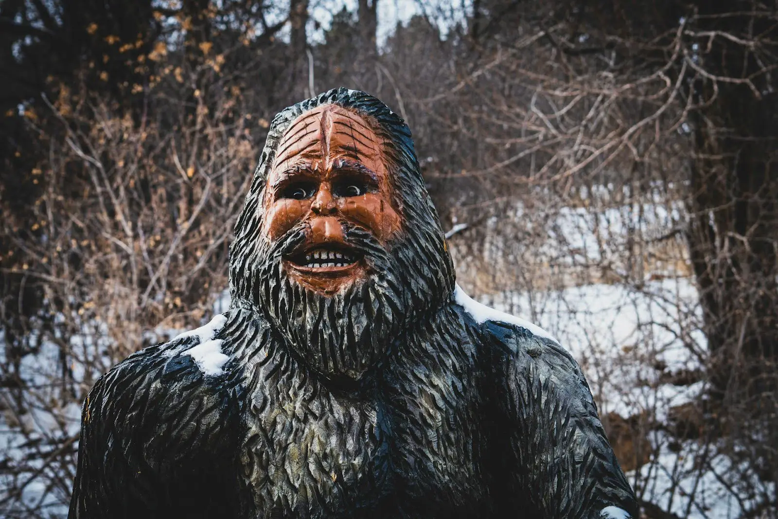 A wooden, painted carved statue of Bigfoot in the snowy woods